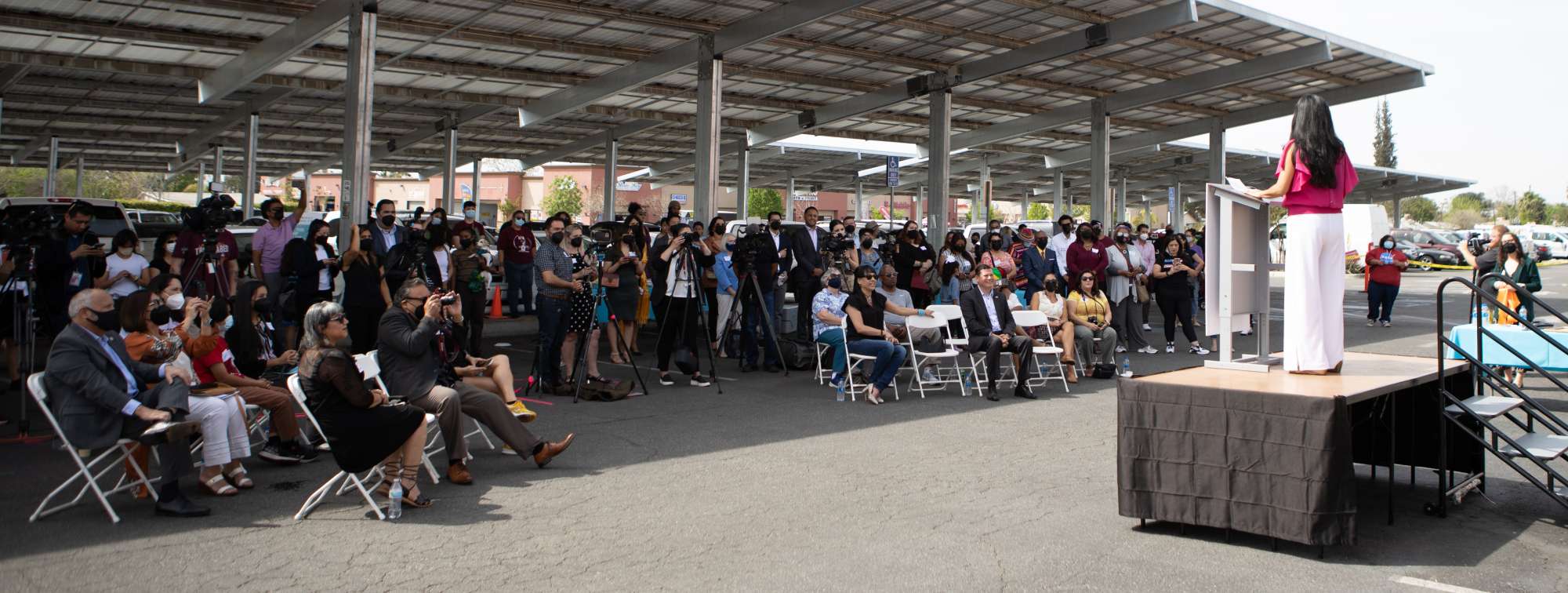 Pictured:  California Impact addressing a gathering seated under an array of solar panels.